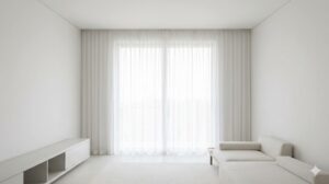 白い壁と一体化するような薄手の白いカーテンが、ミニマルな部屋をより広くすっきりと見せている様子