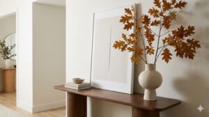 玄関のコンソールテーブルの上に、大きなアートフレームと、紅葉した枝を生けた花瓶が余白を活かして美しく配置されている様子