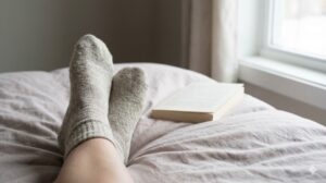 ベッドの上でウールの靴下を履いてリラックスしている足元と、傍らに置かれた本