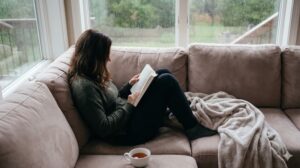 雨の日の窓辺のソファで、ブランケットに包まりながら読書をする女性