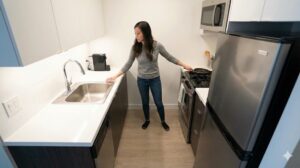 一人暮らしの狭いキッチンで作業動線を確認する女性。シンクとコンロが近い効率的な配置。